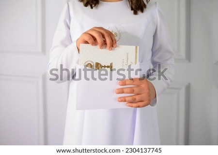 unrecognizable first communion girl putting money received from guests into an envelope. A girl holding in her hands a decorative card with the inscription "Souvenir of the First Holy Communion". Royalty-Free Stock Photo #2304137745