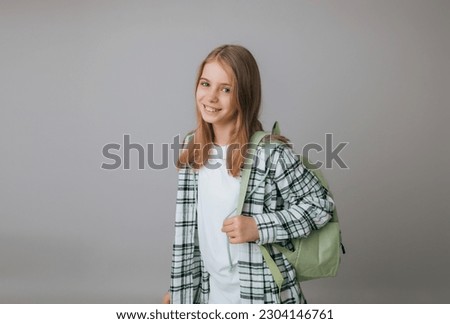 cheerful teenage girl 11,12,13 years old in a school uniform wears a backpack on a gray background. school fashion Royalty-Free Stock Photo #2304146761