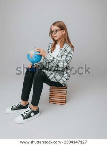 schoolgirl isolated on yellow background with globe. little girl in school uniform sitting on a yellow background, reading a book. blonde girl in school uniform on a yellow background