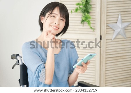 Asian woman in a wheelchair using a smartphone in the living room