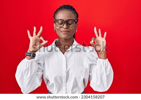 African woman with braids standing over red background relax and smiling with eyes closed doing meditation gesture with fingers. yoga concept. 