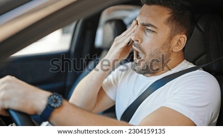 Young hispanic man tired driving car yawning at street Royalty-Free Stock Photo #2304159135