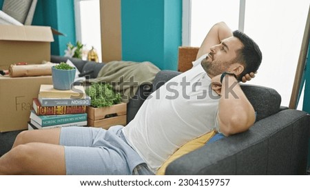 Young hispanic man sitting on sofa with serious expression at new home