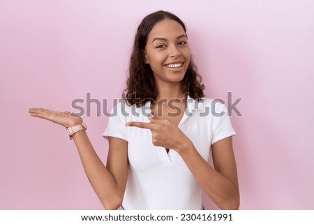 Young hispanic woman wearing casual white t shirt amazed and smiling to the camera while presenting with hand and pointing with finger. 