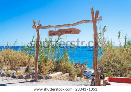 Kamari beach sign at the entrance of the Black Beach,scenic view of Aegean Sea, boats in thw water and Anafi island in the distance,view from Santorini island east coast,Greece.September 5th 2013