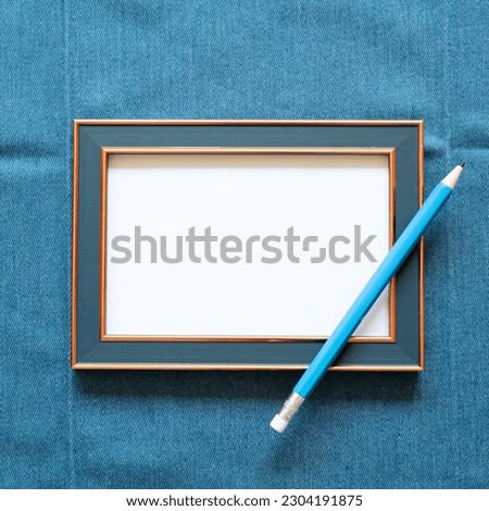 Navy picture frame with white blank paper and pencil on blue fabric background. top view, copy space