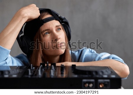 Close-up portrait of a young pretty long-haired DJ girl in a blue sweater and black baseball cap mixing tracks using a DJ console. Music, fun and creativity.