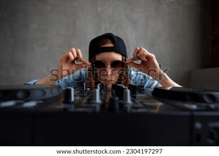 A young pretty long-haired DJ girl in a blue sweater and a black baseball cap is mixing tracks using a DJ console. Music, fun and creativity.