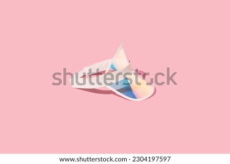 Holographic sports visor hat on sunlight, pink background. Summer vacation relax, sports  accessory, beach hat. Royalty-Free Stock Photo #2304197597