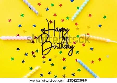The inscription happy birthday on a yellow background. Selective focus, noise. Festive background with candles, confetti in the form of stars with copy space. High quality horizontal photo