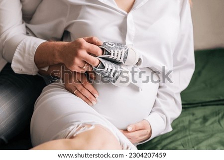 Pregnancy photo shoot, male and female hands and baby booties Royalty-Free Stock Photo #2304207459