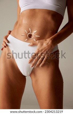 Woman apply sun cream. Cropped image with slim female body with tanned skin in underwear with suntan lotion on belly over studio background. Sun protection cream. Concept of health, vacation, spf