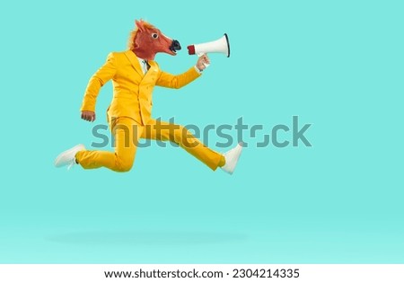 Full body side view young man in trendy yellow suit and funny crazy masquerade carnival horse face mask jumps up, flies on blue studio background, makes announcement through megaphone with loud voice Royalty-Free Stock Photo #2304214335