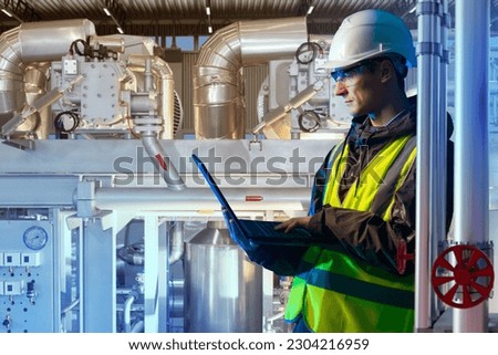 Production engineer. Technologist with laptop. Man works in factory. Engineer near industrial equipment. Chemical production. Master maintains industrial equipment. Man jobs in chemical plant Royalty-Free Stock Photo #2304216959
