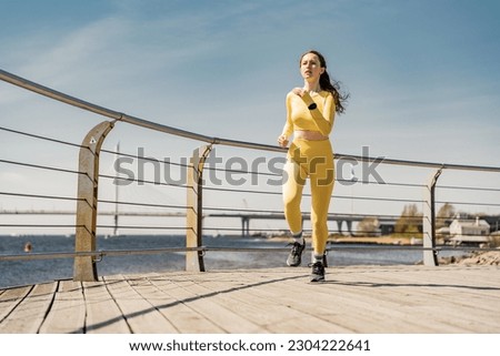 A healthy lifestyle and cardio fitness watch on the arm, a strong female runner in sportswear, trains alone in sneakers. Full-length doing a workout in the park.