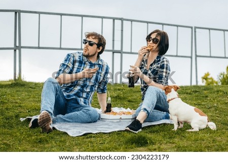 Young family with their dog sitting on the grass and eating pizza snack outdoor Royalty-Free Stock Photo #2304223179