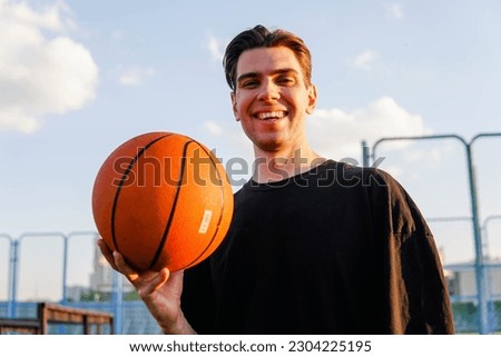 Young brunette man holding basketball ball looking positive and happy standing and smiling with a confident smile showing teeth