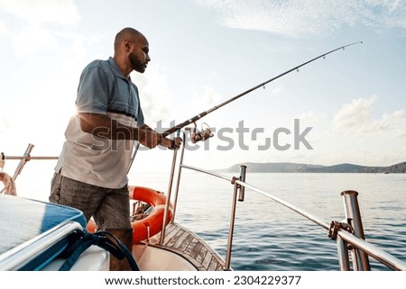 Young african american man standing with fishing rod on a sailboat fishing in open sea on sunset Royalty-Free Stock Photo #2304229377