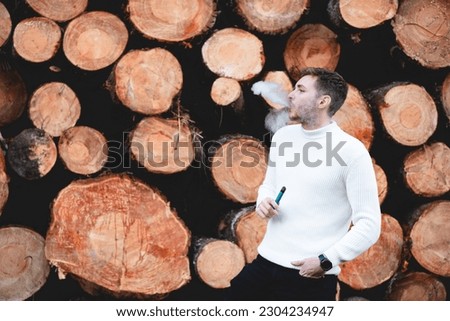 Young boy smoking vaper, vaping next to some wooden logs. Health concept, vaping.