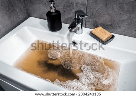 Clogged sink in bathroom, sink with dirty water, brown soap. Plumbing problems. Royalty-Free Stock Photo #2304243135