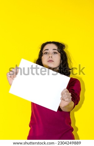 A latin woman holding a white piece of paper in front of her face