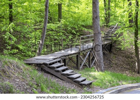 Wooden old footbridge over a ravine with crumbling steps in a public park on a sunny spring day.