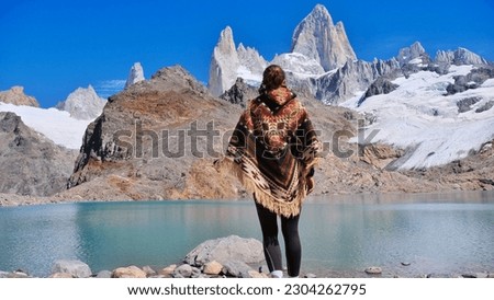 Trekking brunette girl wearing traditional peruvian poncho in the andes mountain looking at Fitz Roy peak near El Chalten, Patagonia, Argentina