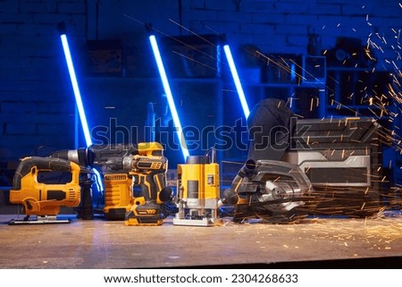 electric power tools are on the workbench in the workshop: a jigsaw, a drill, a hammer drill, a screwdriver, a milling cutter, a circular saw. sparks fly from the side Royalty-Free Stock Photo #2304268633