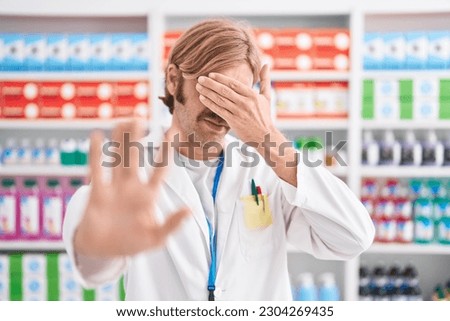 Caucasian man with mustache working at pharmacy drugstore covering eyes with hands and doing stop gesture with sad and fear expression. embarrassed and negative concept. 