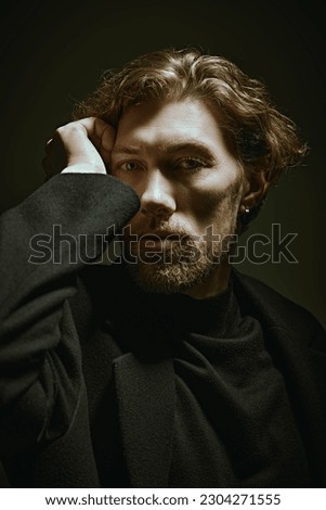 Art portrait in a dark key of a handsome forty-year-old man with curly hair, dressed in a black pullover and a jacket, who looks thoughtfully at the camera. People, emotions. Psychological picture.