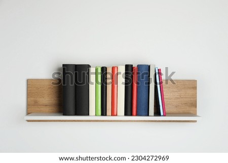 Different books on wooden shelf near white wall
