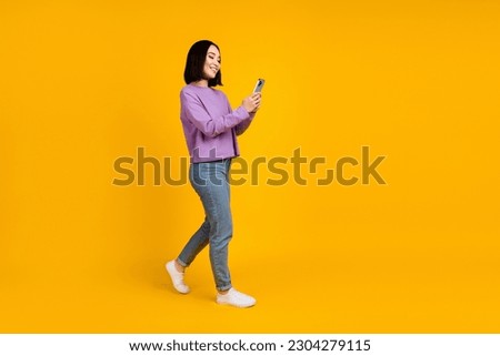 Full body size photo of young chinese blogger girl hold phone walking recording video online popularity isolated on yellow color background