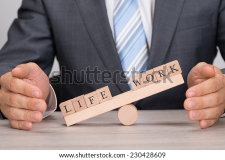 Midsection of businessman covering imbalance between Life and Work on seesaw at table