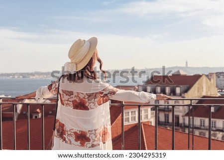 Woman in a straw hat looking over the rooftops of the Lisbon town  Royalty-Free Stock Photo #2304295319