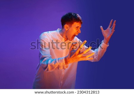 Portrait of young emotional man, expressively shouting, screaming against gradient purple background in neon light. Anger, annoyance. Concept of human emotions, lifestyle, youth