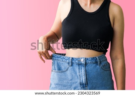 Diet and weight loss concept. Young Asian woman body in oversize jeans on pink pastel background.
