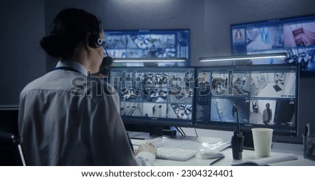 Female security officer watches security cameras with AI facial recognition with male colleagues. Monitoring center workers. Computer monitors and big digital screens with CCTV cameras video footage. Royalty-Free Stock Photo #2304324401
