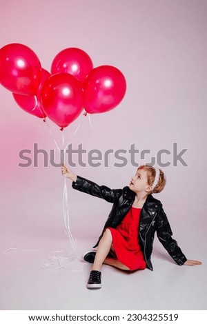 Stylish girl smiles toothlessly, wears a black leather jacket and balloons, has fun with her best friends, isolated on a pink background. Children, holiday concept, birthday.