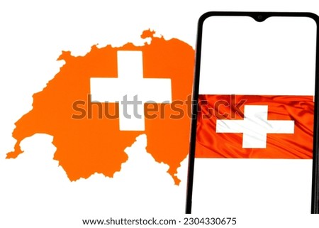 Swiss Flag displayed on mobile phone, Switzerland map blurred in the background.