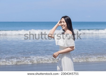 Beautiful young woman asian standing on the beach with hands touch head. Close up face of young tanned woman with closed eyes enjoying breeze at seaside.