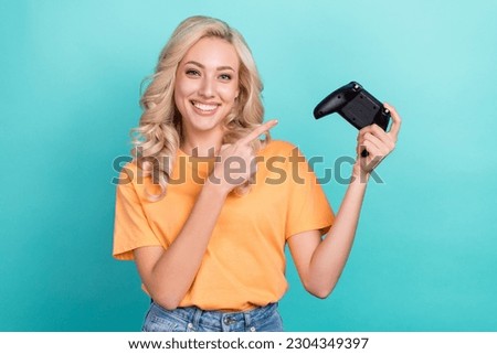 Photo of optimistic cheerful girl with wavy hairstyle dressed yellow t-shirt directing at joystick isolated on teal color background