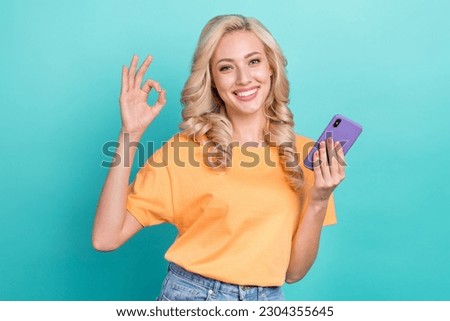Portrait of friendly lovely person wavy hairdo wear stylish t-shirt hold smartphone showing okey isolated on turquoise color background