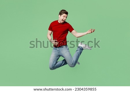 Full body singer young brunet man he wearing red t-shirt casual clothes jump high pretend playing guitar, sing song isolated on plain pastel light green background studio portrait. Lifestyle concept Royalty-Free Stock Photo #2304359855
