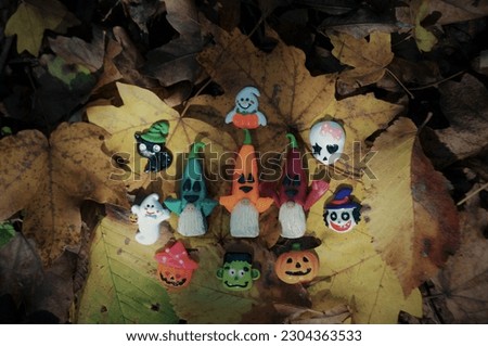 Funny figures of Halloween-themed characters. Gnomes, ghost, cat, pumpkin. Toys on the background of autumn leaves.