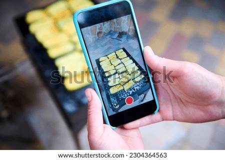 Female hands holding mobile phone in live view mode and taking photos of tasty yummy marinated vegetables grilling over charcoal in the barbecue grill in the backyard. Summer picnic concept. Chill out