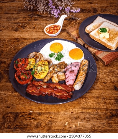 English Breakfast in cooking pan with fried eggs, sausages, bacon, beans, toasts on dark stone background copy space