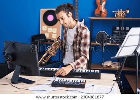 Young hispanic man musician composing song holding trumpet at music studio Royalty-Free Stock Photo #2304381877