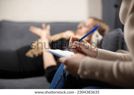 Female cient lying on couch shares childhood traumas with psychologist. Expert simultaneously records important details from patient life Royalty-Free Stock Photo #2304383635