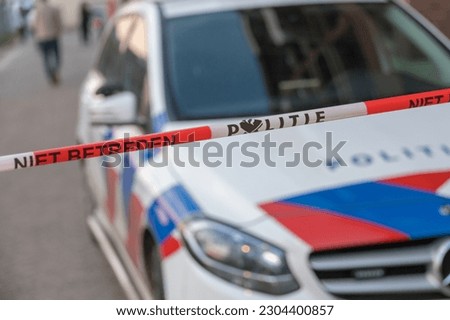 Politie, Dutch police. Close up of barrier tape or afzetlint with text: 'niet betreden'. Translation: do not cross or enter. Crime scene, investigation. Police car in background. Part of a serie. Royalty-Free Stock Photo #2304400857