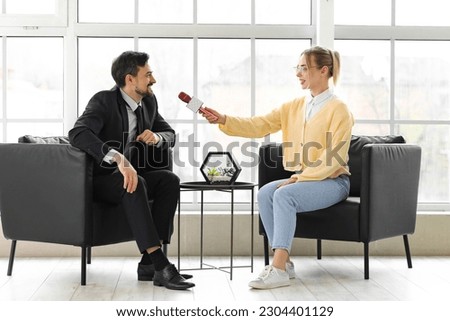 Female journalist with microphone having an interview with man in office Royalty-Free Stock Photo #2304401129